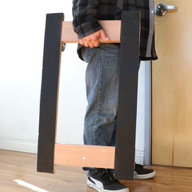 A person is using a solid wood furniture moving dolly with black rubber tread on the caster wheels for anti-slip protection. The dolly has a pre-assembled platform and is designed for easy transportation of furniture.